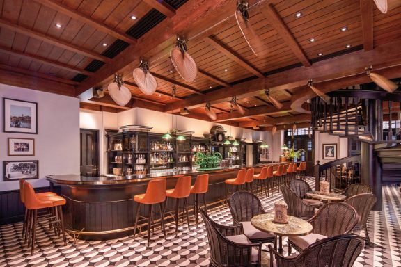 Elegante Bar mit Holzdecke, Stühlen in Orange und schwarz-weißem Boden.