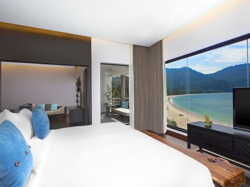 Modernes Hotelzimmer mit großer Fensterfront und Blick auf den Strand und die Berge.