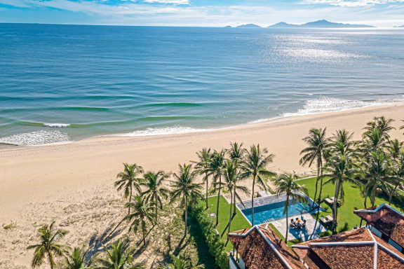 Tropischer Strand mit Palmen, Pool und Meerblick unter blauem Himmel.