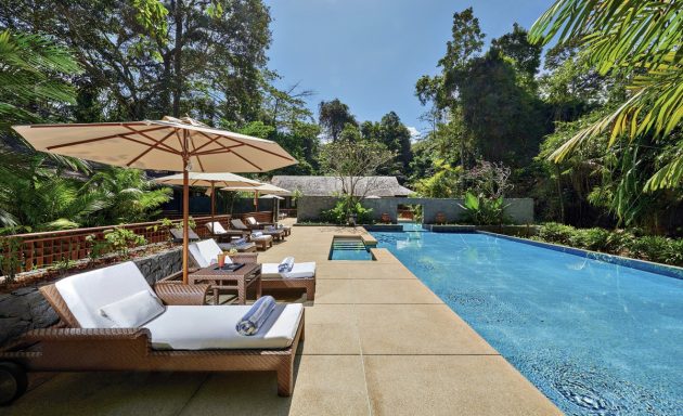 Klarer Poolbereich mit Liegen und Sonnenschirmen, umgeben von üppiger Vegetation.