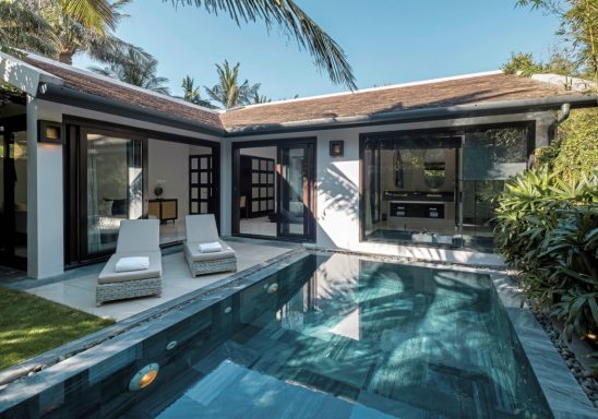 Moderne Villa mit privatem Pool und Liegen, umgeben von Palmen und Grünflächen.