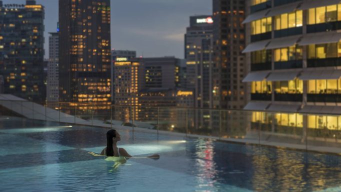 Dunkler Stadtblick mit Rooftop-Pool und einer Person im Wasser.