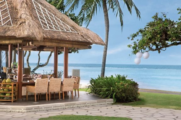 Tropische Strandlandschaft mit einem Essbereich unter einem traditionellen Dach.