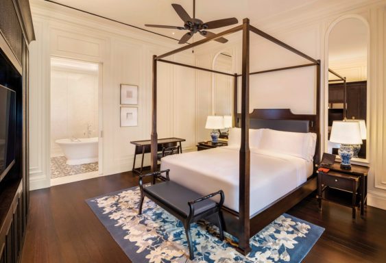 Helles Schlafzimmer mit Himmelbett, Schreibtisch und großem Flachbildfernseher.