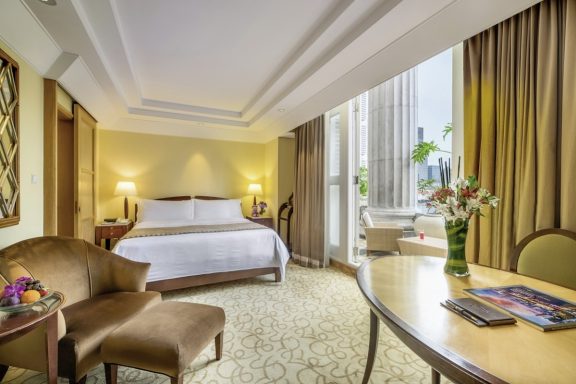 Helles Hotelzimmer mit Doppelbett, Sitzgelegenheit und Blick auf die Stadt.