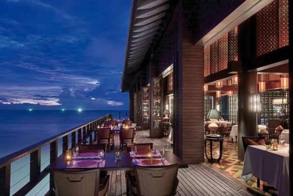 Elegantes Restaurant am Wasser bei Dämmerung, mit Tischen und sanfter Beleuchtung.