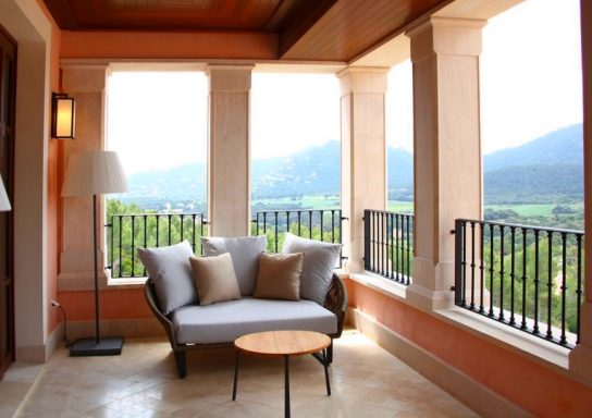 Gemütlicher Balkon mit Sofa, Tisch und Blick auf grüne Berge und Tal.