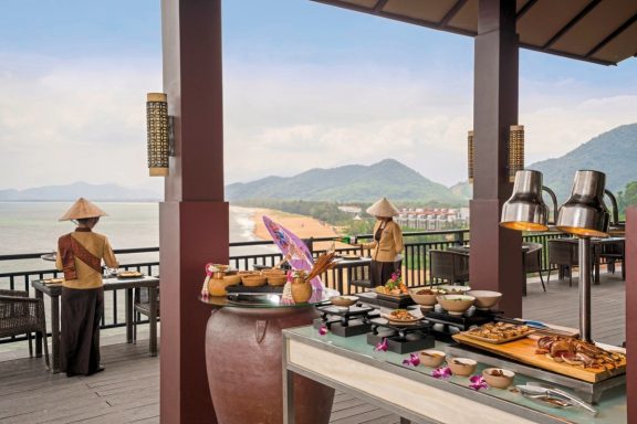 Buffet mit verschiedenen Speisen, Blick auf Landschaft und Wasser im Hintergrund.