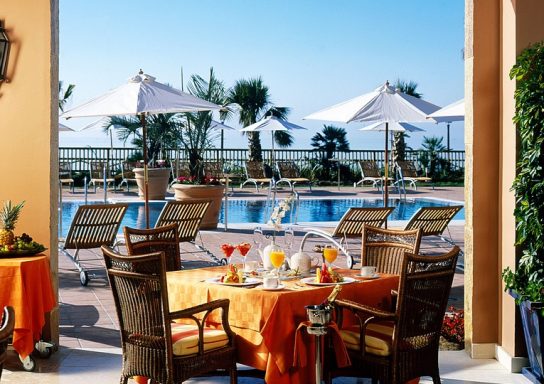 Ein eleganter Frühstückstisch mit Blick auf einen Pool und Sonnenschirme im Hintergrund.