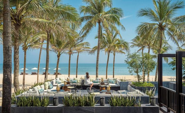 Tropische Landschaft mit Palmen, Strand und einem Outdoor-Speisebereich.