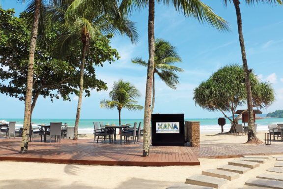 Tropischer Strand mit Palmendäumen, Tischen und Stühlen, Blick aufs Meer.