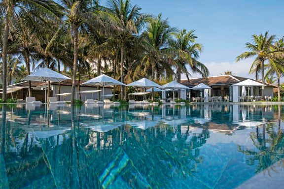 Eleganter Poolbereich mit Liegen und Palm Trees vor einem luxuriösen Resort.