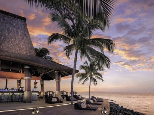 Luxuriöse Strandbar bei Sonnenuntergang, umgeben von Palmen und einer ruhigen Meeresfläche.