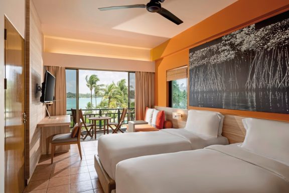 Moderne Hotelzimmer mit zwei Betten, Balkon und Blick auf die Palmenlandschaft.