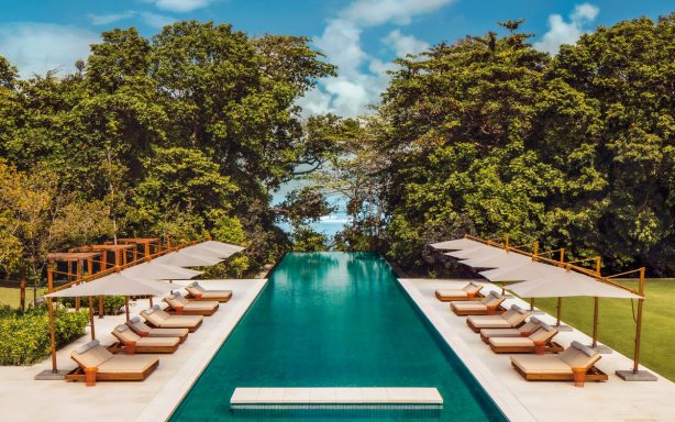 Eleganter Swimmingpool mit Liegen, umgeben von üppigem Grün und blauem Himmel.