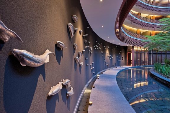 Ein modern gestalteter Innenraum mit einem gewundenen Wasserlauf und Fischskulpturen an der Wand.