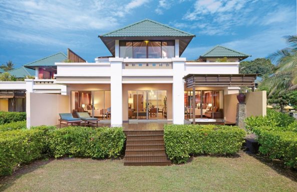 Moderne Villa mit grünem Rasen, Terrasse und schattigem Vordach unter blauem Himmel.