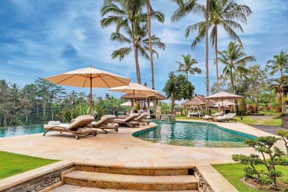 Luxuriöser Außenbereich mit Pool, Liegen und Sonnenschirmen umgeben von Palmen.