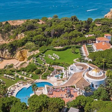 Elegantes Sheraton Mallorca - Arabella Golfresort mit Gartenlandschaft und einem Sandplatz im Vordergrund.