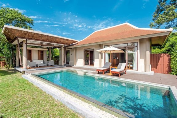 Moderne Villa mit Pool, Liegen und überdachter Veranda in einer grünen Umgebung.