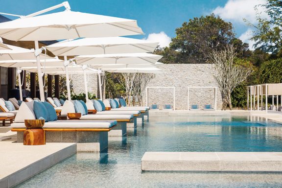 Schöner Poolbereich mit Liegen und Sonnenschirmen umgeben von Grünpflanzen.