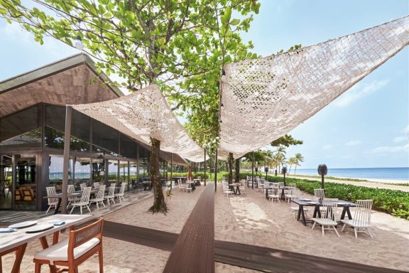 Helle Restaurantterrasse mit Sonnenschirmen und Blick auf das Meer.