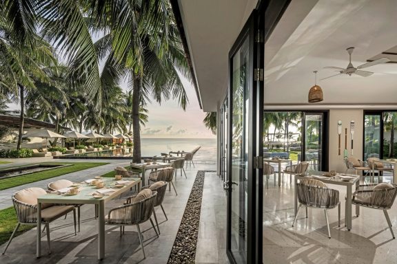 Elegante Restaurantterrasse mit Blick auf den Pazifischen Ozean und palmengesäumten Garten.