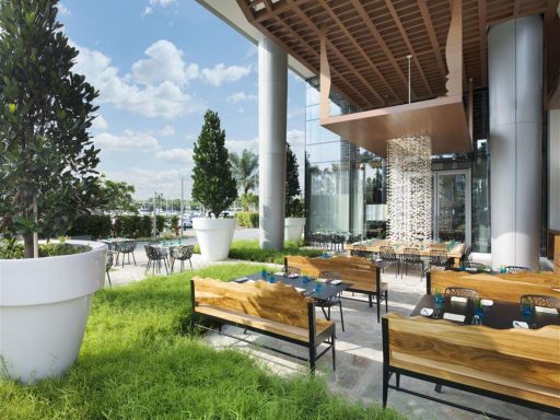 Moderne Terrasse mit Holzbänken und grüner Rasenfläche, umgeben von Pflanzen.