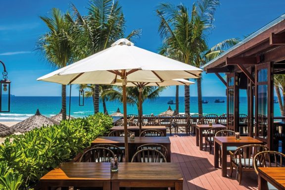 Entspannte Terrasse mit Tischen, Sonnenschirmen und Blick auf das Meer.