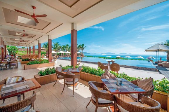 Helles Restaurant mit Blick auf das Meer und tropische Pflanzen. Sonnenschein und Palmen.